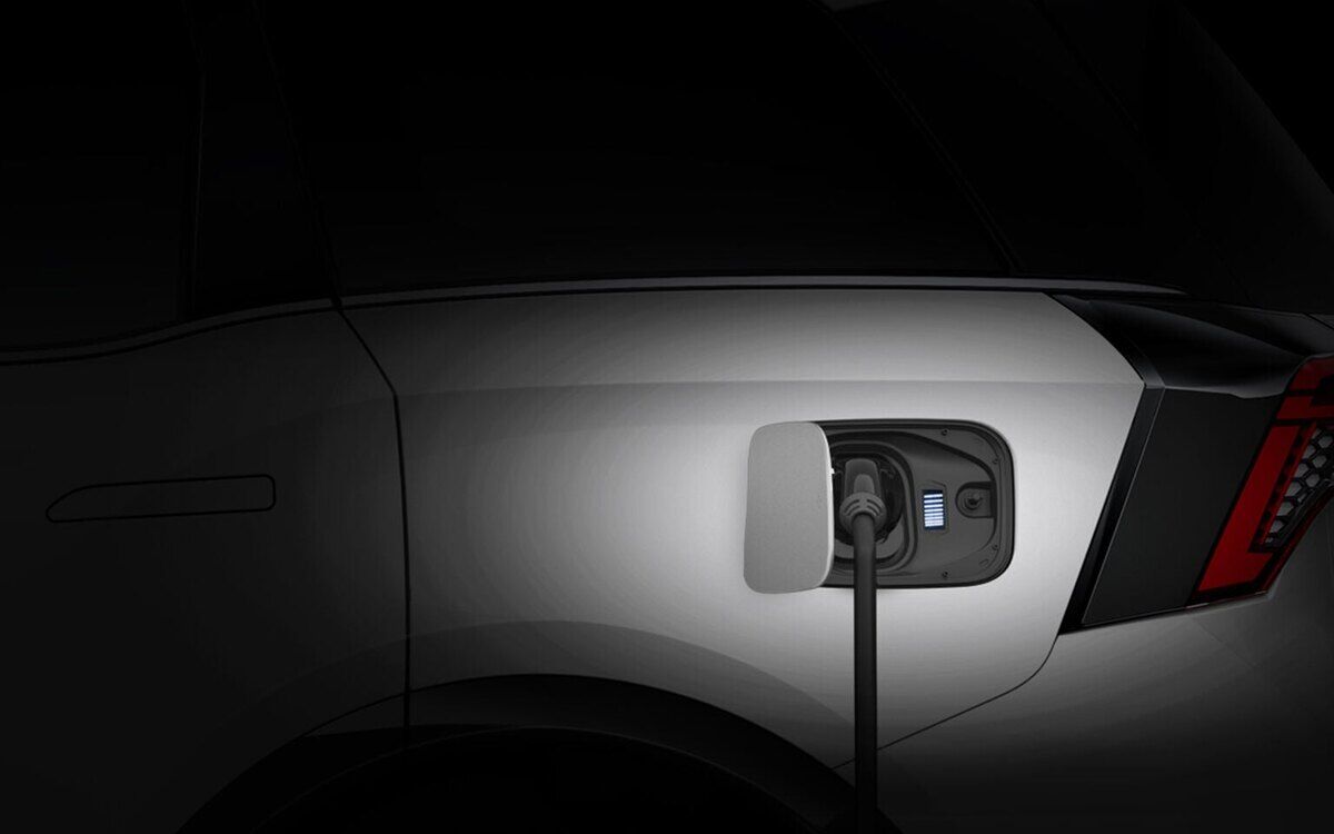 A white Mahindra XEV 9S plugged in to charge, close-up of the rear side and charging port with the connector cable, against a dark background