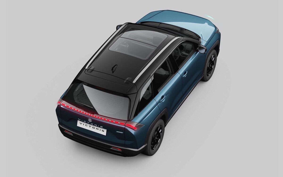 A blue Maruti Suzuki Victoris with a black roof and panoramic glass, seen from above at the rear three-quarter angle on a plain grey studio background