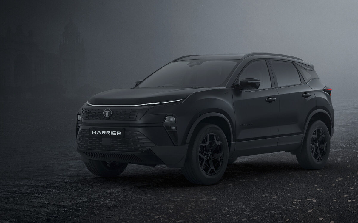 A matte-black Tata Harrier Stealth edition, front three-quarter view, parked on dark cracked tarmac in thick fog, with the faint outline of a domed building behind