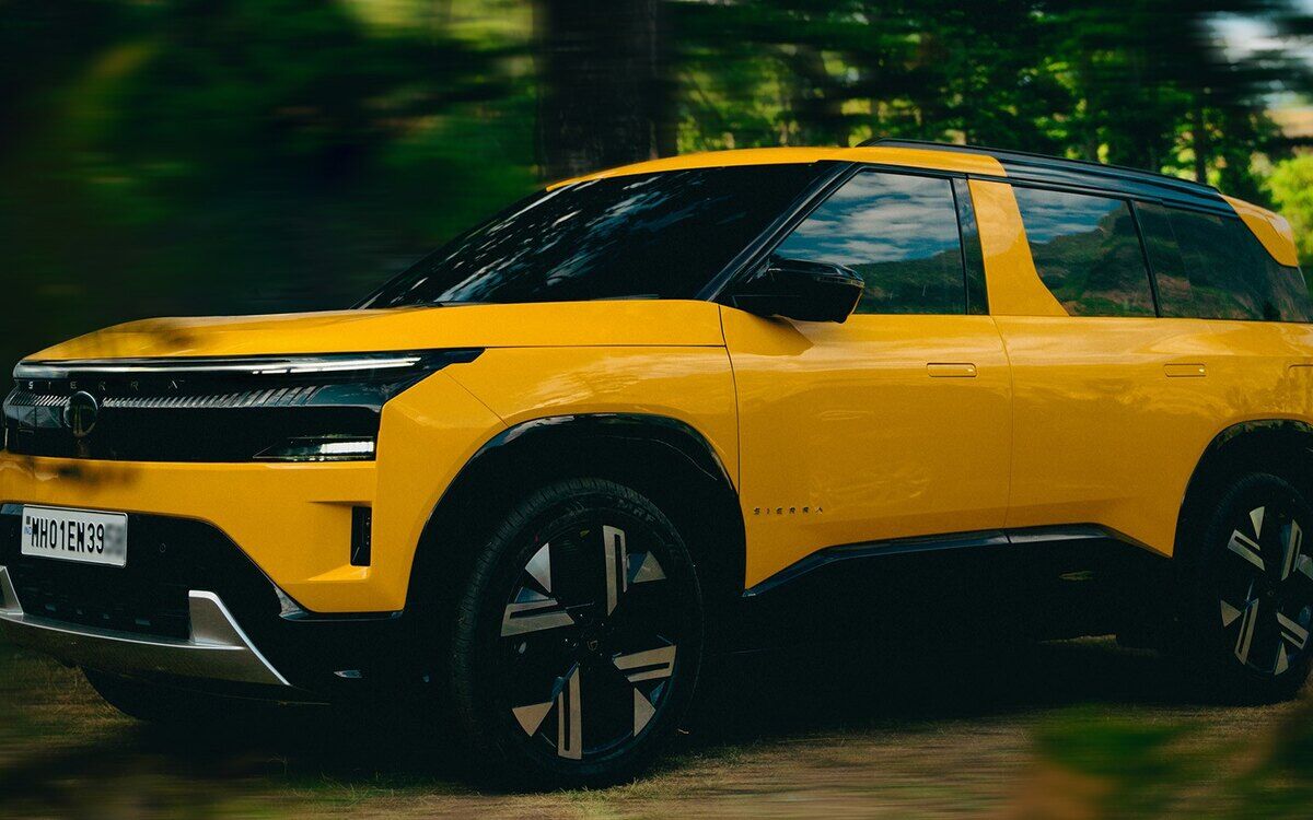 A yellow Tata Sierra with a black roof and dark alloy wheels, front three-quarter view, driving along a forest track