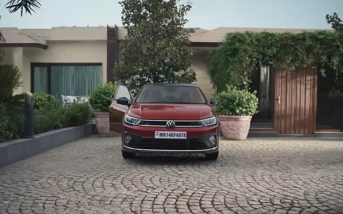 Front view of a red Volkswagen Virtus GT parked on a cobbled driveway outside a house, driver's door open