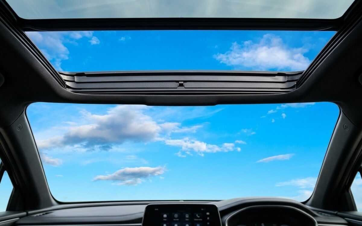 Blue sky seen through an open panoramic sunroof from inside a car