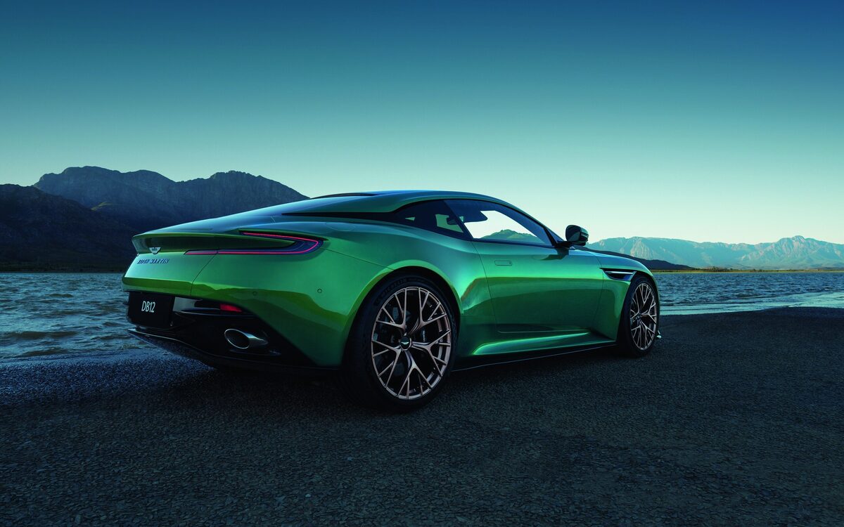 Green Aston Martin DB12 parked by a lake, rear three-quarter view