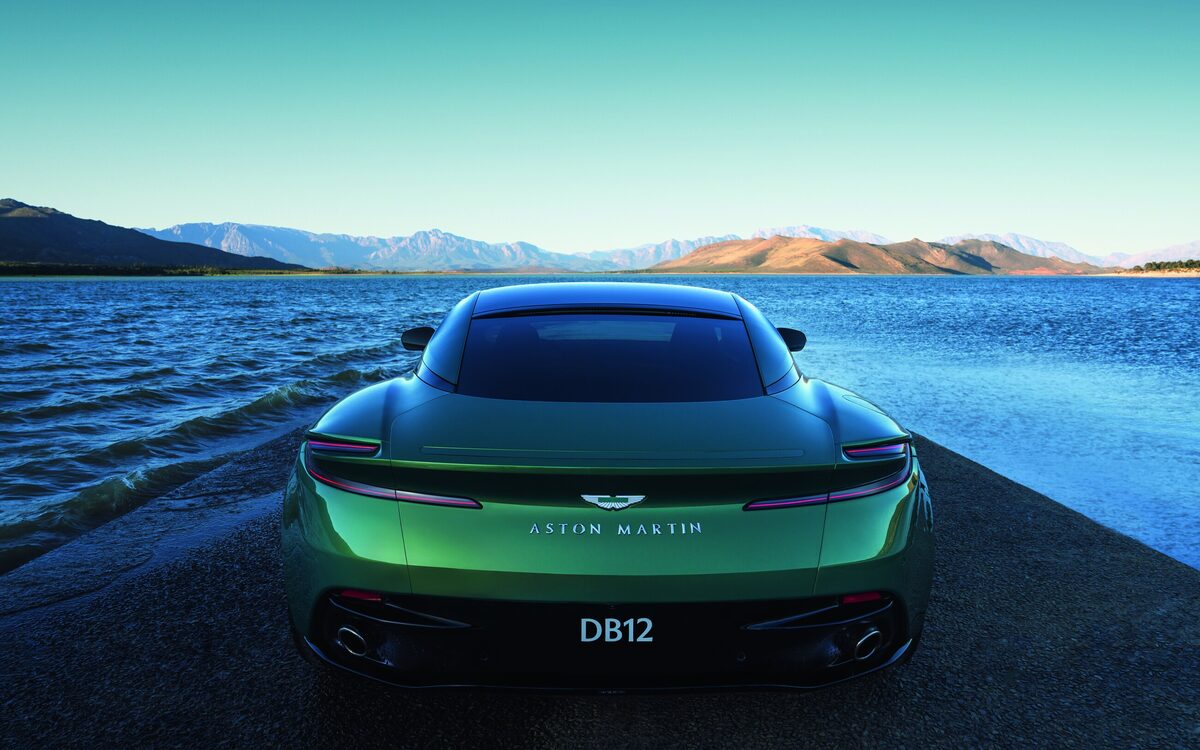 Green Aston Martin DB12 seen directly from behind with the DB12 badge, lake in the background