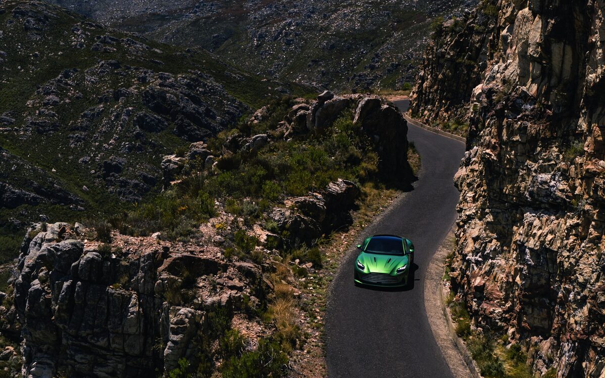 Green Aston Martin DB12 on a winding mountain road seen from above