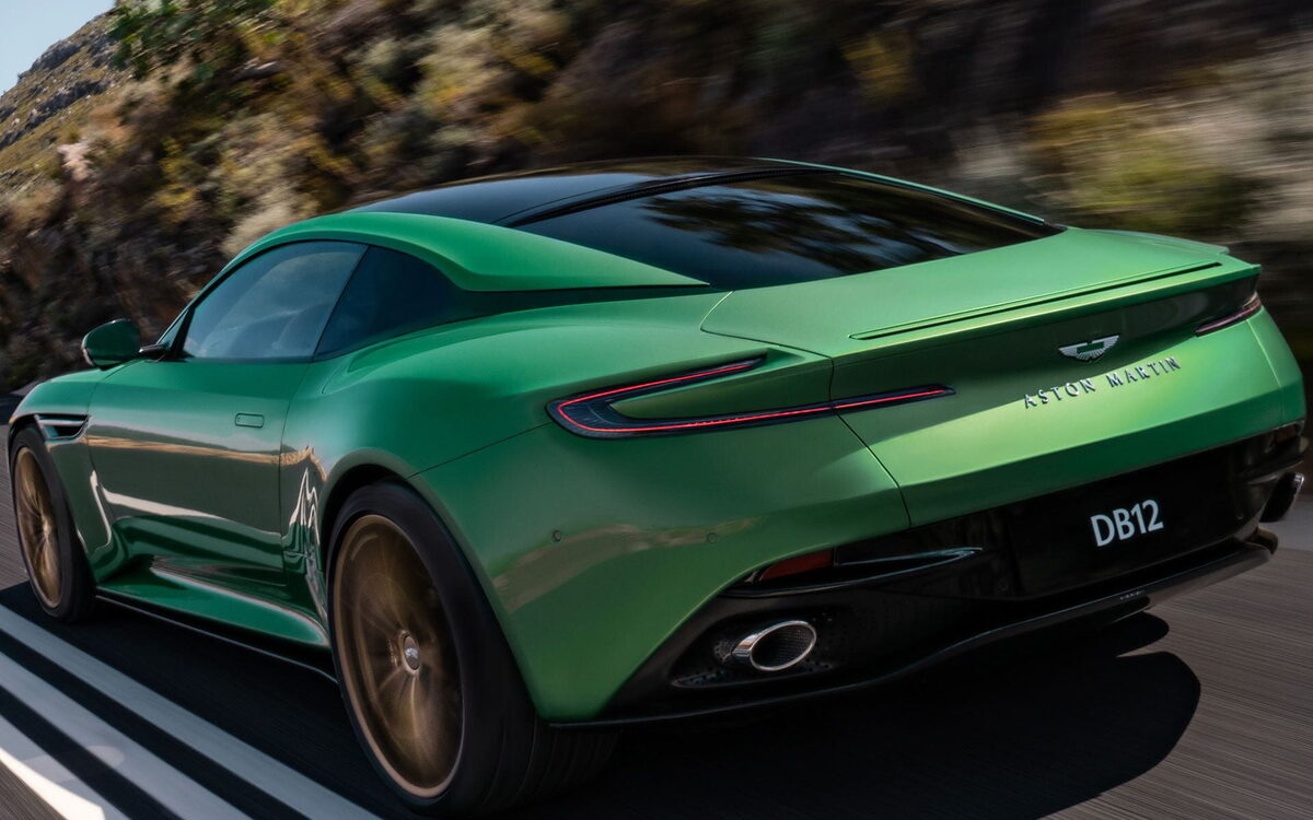 Green Aston Martin DB12 cornering on a mountain road, rear three-quarter view