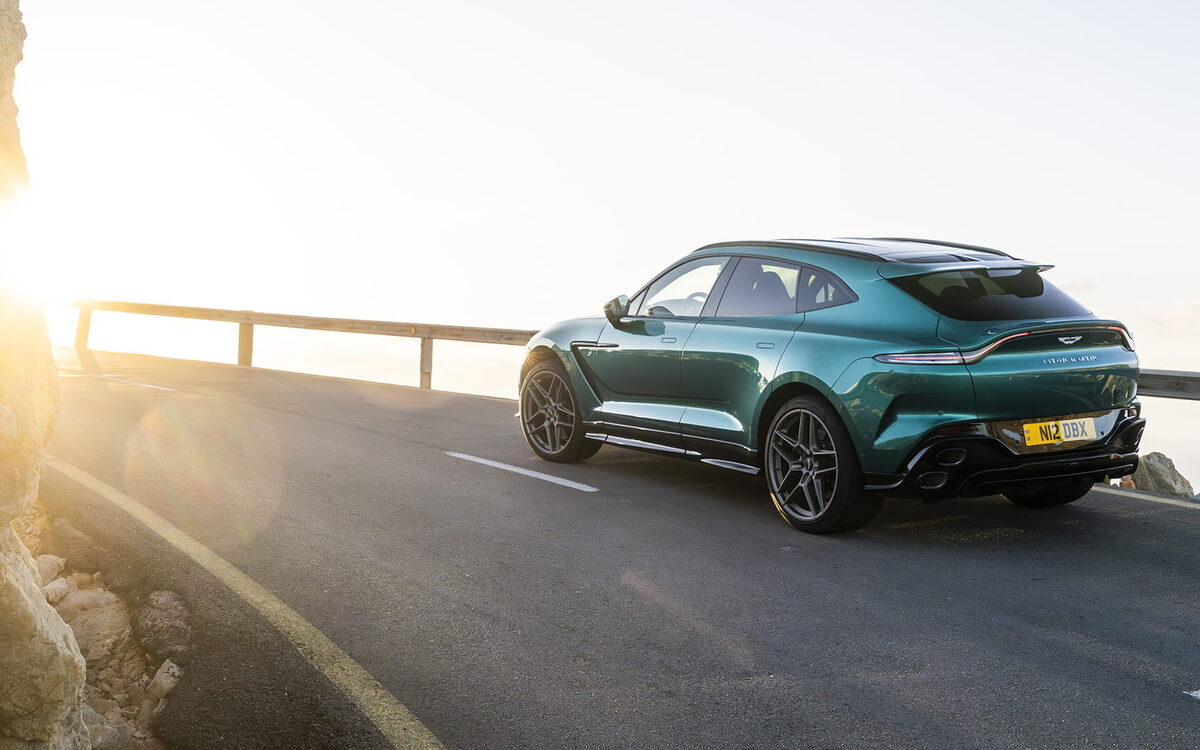 Teal Aston Martin DBX S at sunset on a mountain road, rear three-quarter view