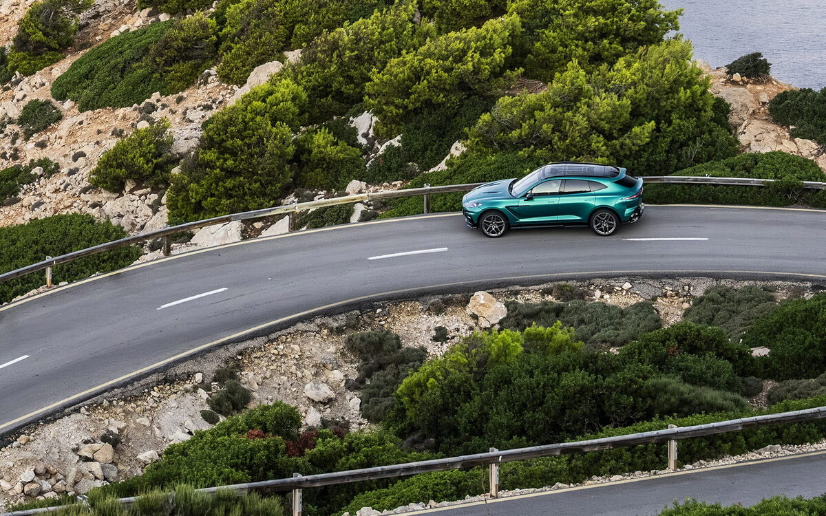 Teal Aston Martin DBX S on a winding coastal road seen from above