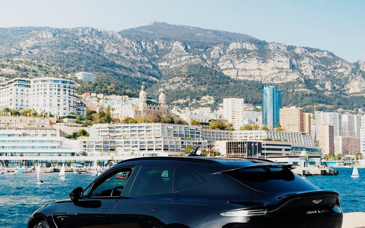 Black Aston Martin DBX S with red accents parked on a seafront, rear three-quarter view
