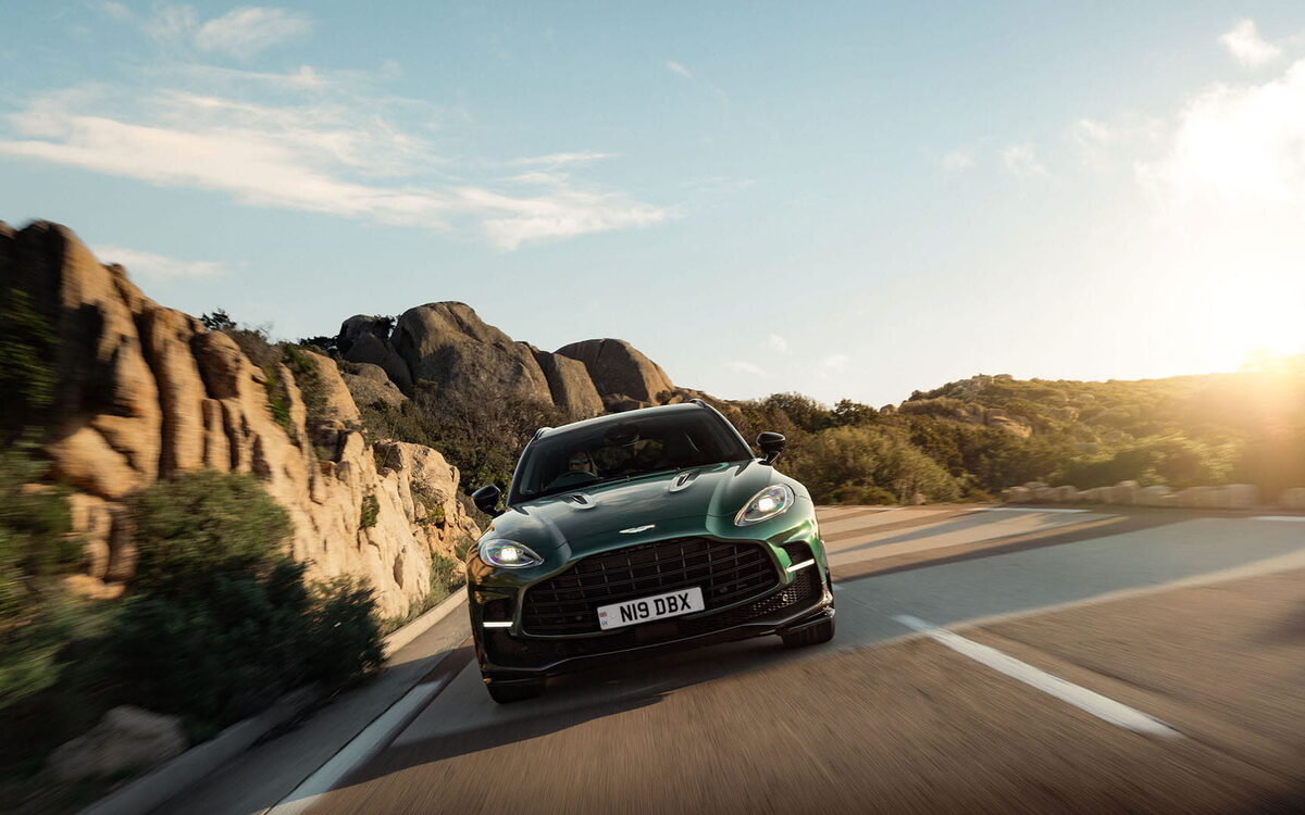 Green Aston Martin DBX707 driving on a coastal road in warm sunlight, front view