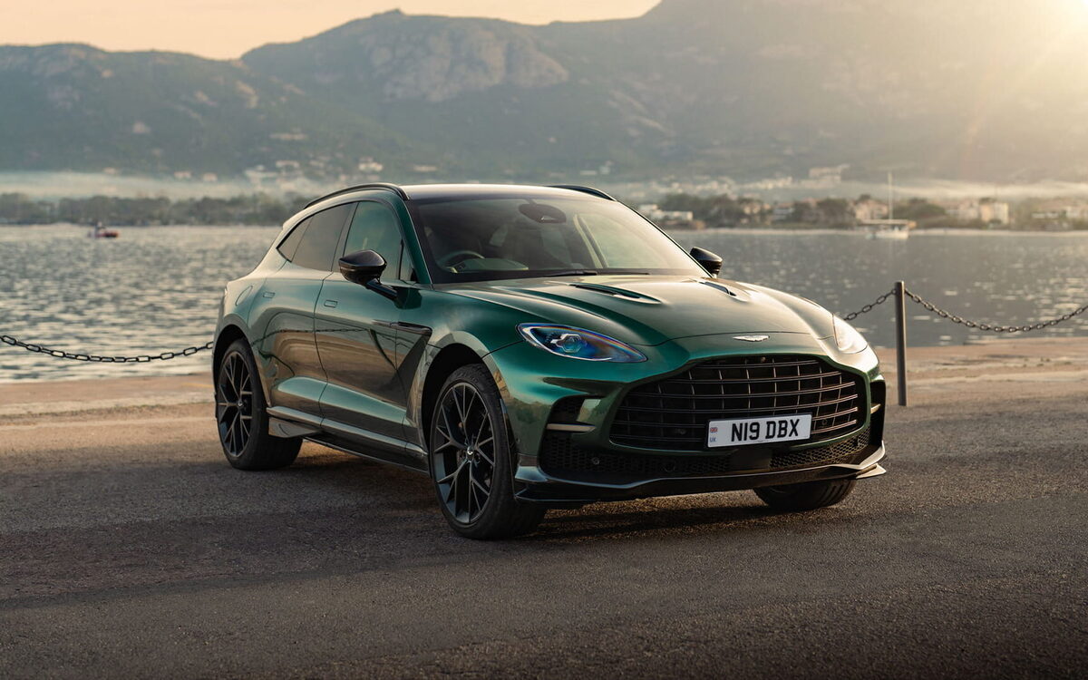 Dark green Aston Martin DBX707 parked on a beach at sunset, front three-quarter view