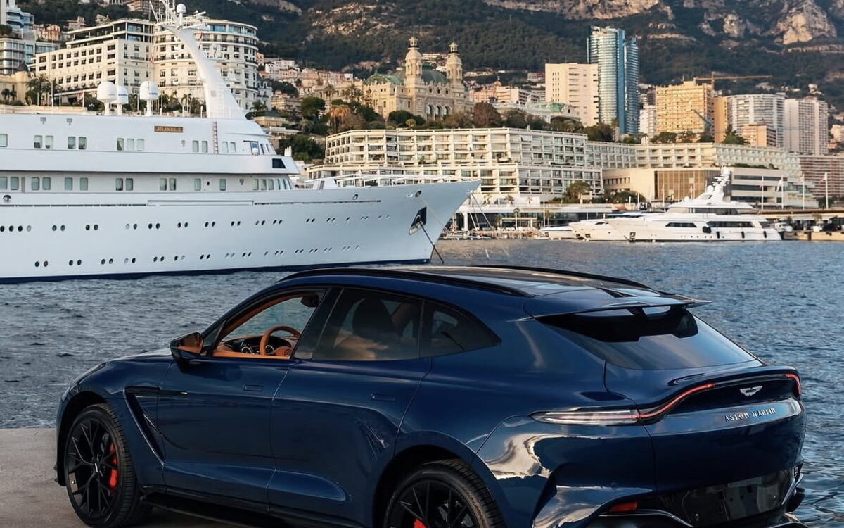 Dark blue Aston Martin DBX707 parked by a harbour, rear three-quarter view