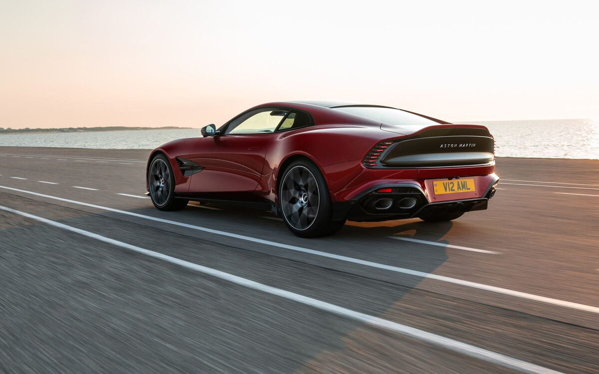 Red Aston Martin Vanquish on a coastal road at sunset, rear three-quarter view