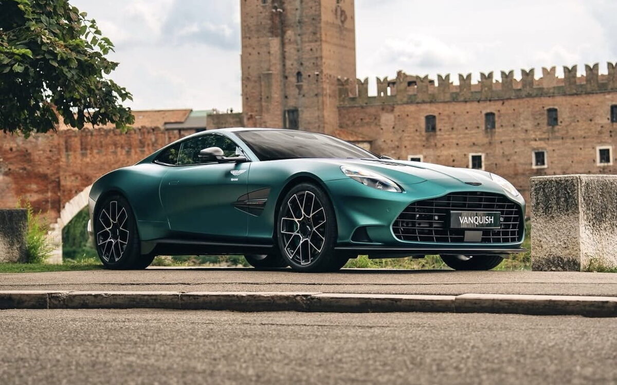 Green Aston Martin Vanquish parked in front of an old brick tower, front view