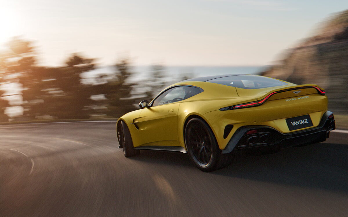 Yellow Aston Martin Vantage driving fast, rear three-quarter view