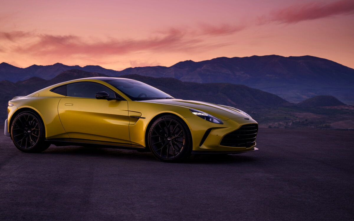 Yellow Aston Martin Vantage at dusk with mountains behind, side three-quarter view