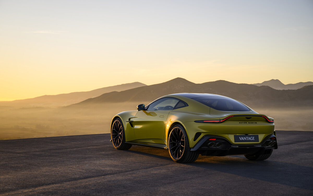 Yellow Aston Martin Vantage in a desert landscape at sunset, rear three-quarter view