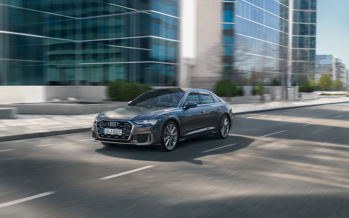 Audi A6 in Chronos Grey driving through a city, front three-quarter view in motion