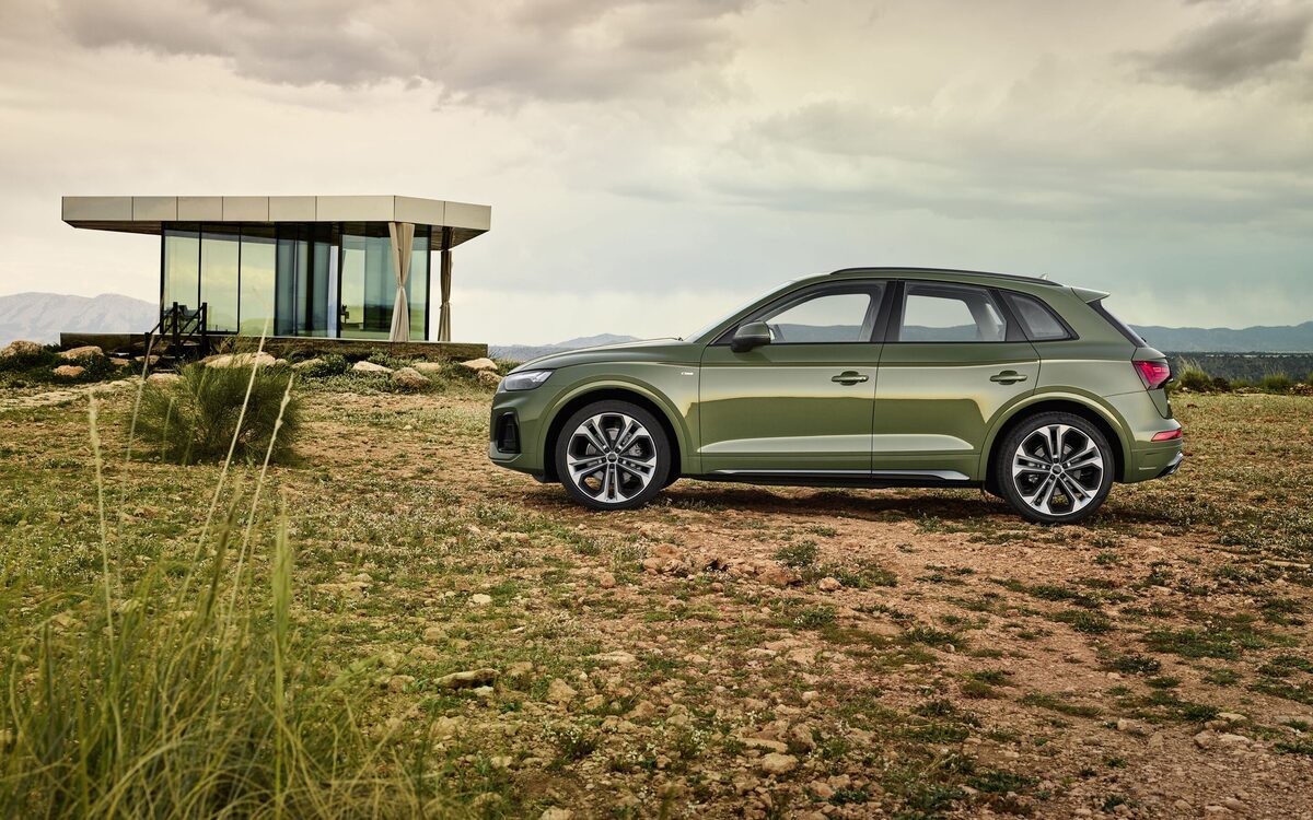 Audi Q5 in District Green, side profile on open ground with a glass pavilion behind