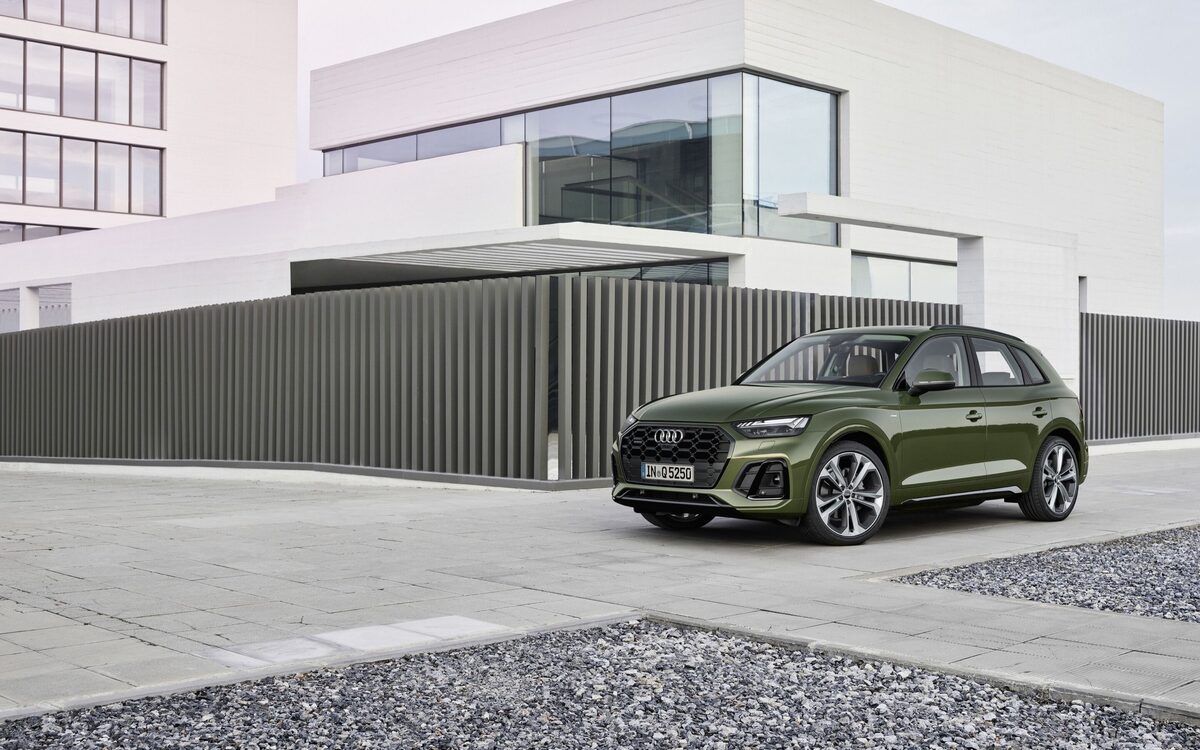 Audi Q5 in District Green, front three-quarter view parked on a paved forecourt beside a modern building