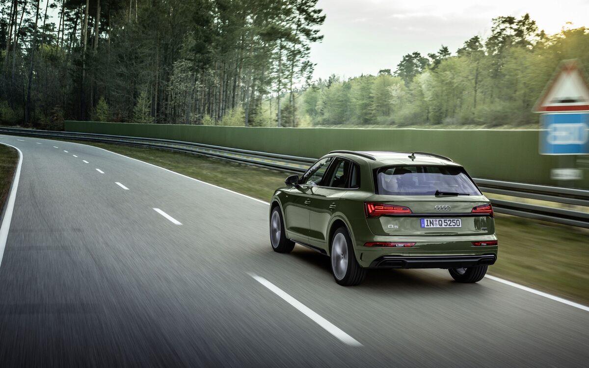 Audi Q5 in District Green, rear three-quarter view driving along a straight road lined with trees