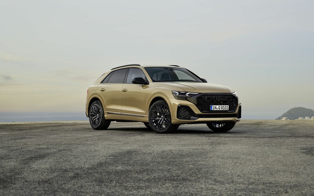 Audi Q8 in Sakhir Gold, front three-quarter view parked on open tarmac under a pale sky