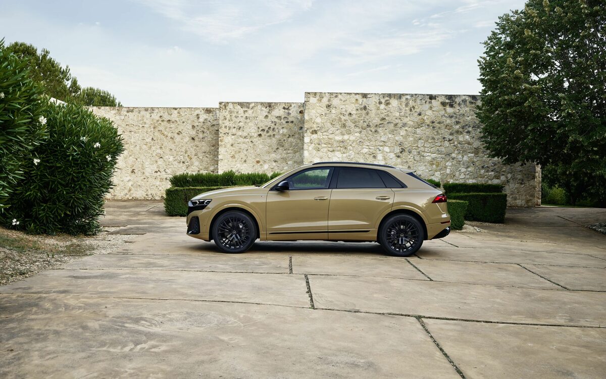 Audi Q8 in Sakhir Gold, side profile parked on a paved courtyard in front of a stone wall