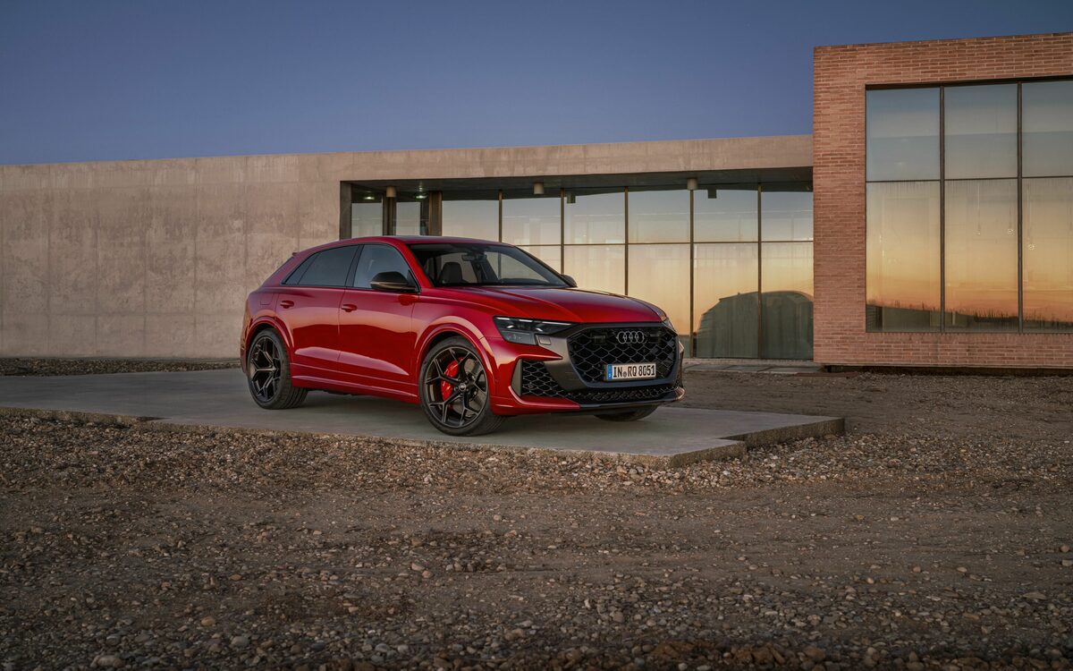 Audi RS Q8 performance in Chili Red, front three-quarter view parked on a gravel forecourt in front of a glass building