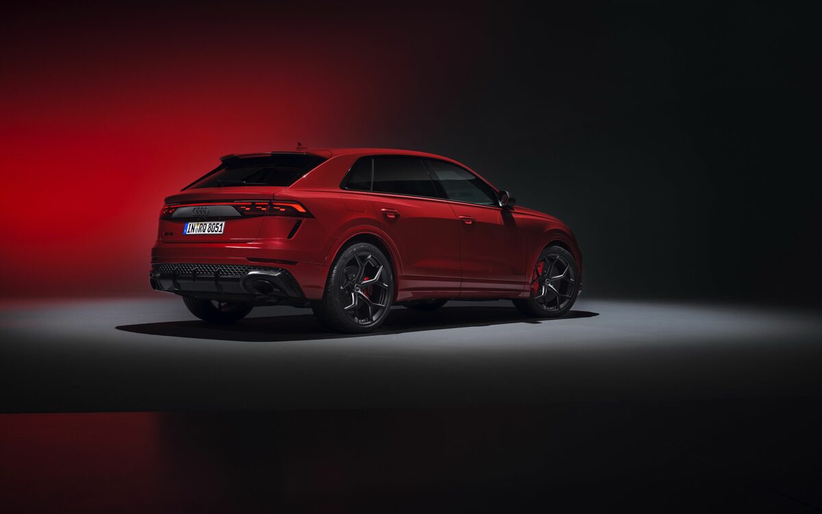 Audi RS Q8 performance in Chili Red, rear three-quarter view in a dark studio with red backdrop