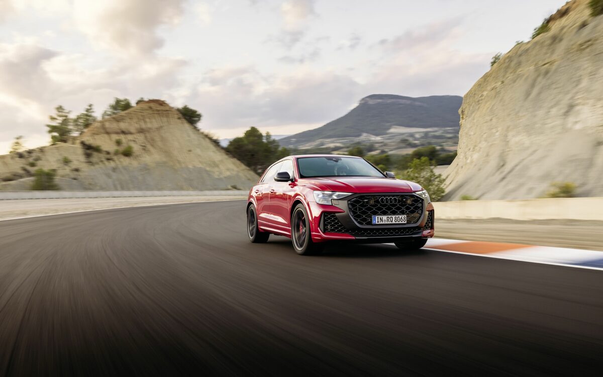 Audi RS Q8 performance in Chili Red, front three-quarter view driving fast through a rocky hill road