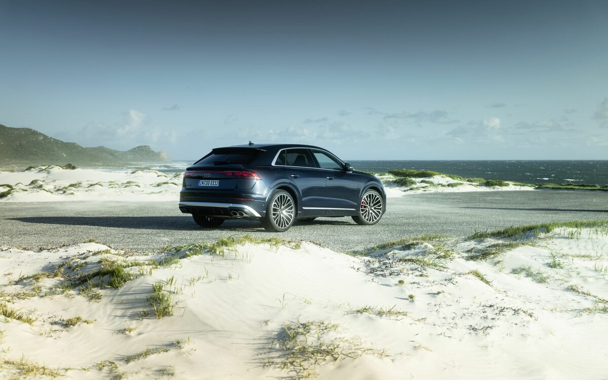 Audi SQ8 in Waitomo Blue, rear three-quarter view parked on a dune-side coastal road