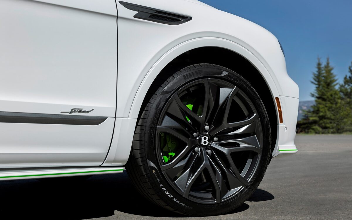 Close-up of the black alloy wheel with green brake caliper on a white Bentayga Speed