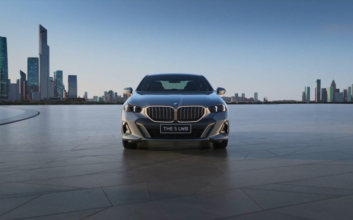 BMW 5 Series Long Wheelbase front view on an open plaza with a city skyline behind