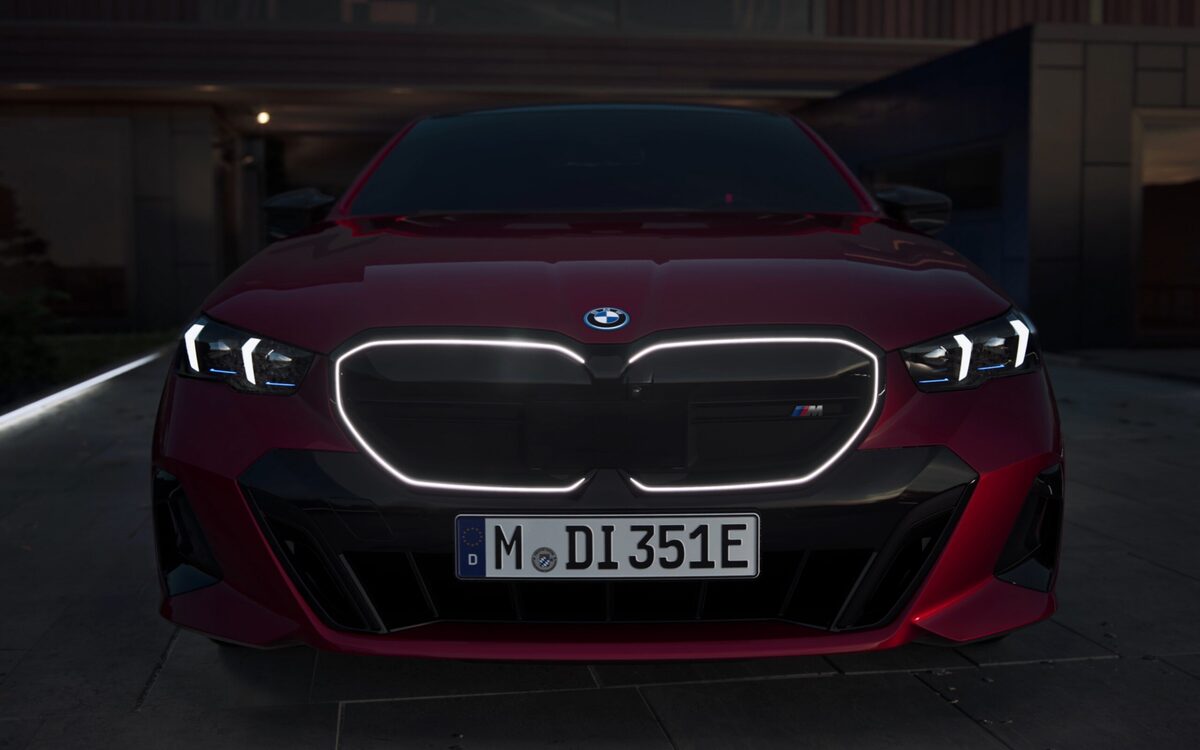 BMW i5 M60 in Fire Red seen from the front, with the illuminated kidney grille and sharp headlamps