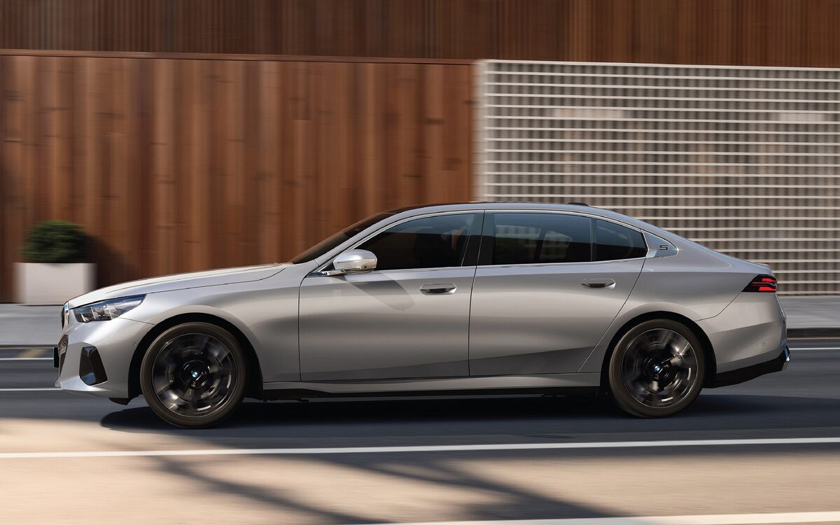 BMW i5 LWB side profile in silver, driving past a wooden wall
