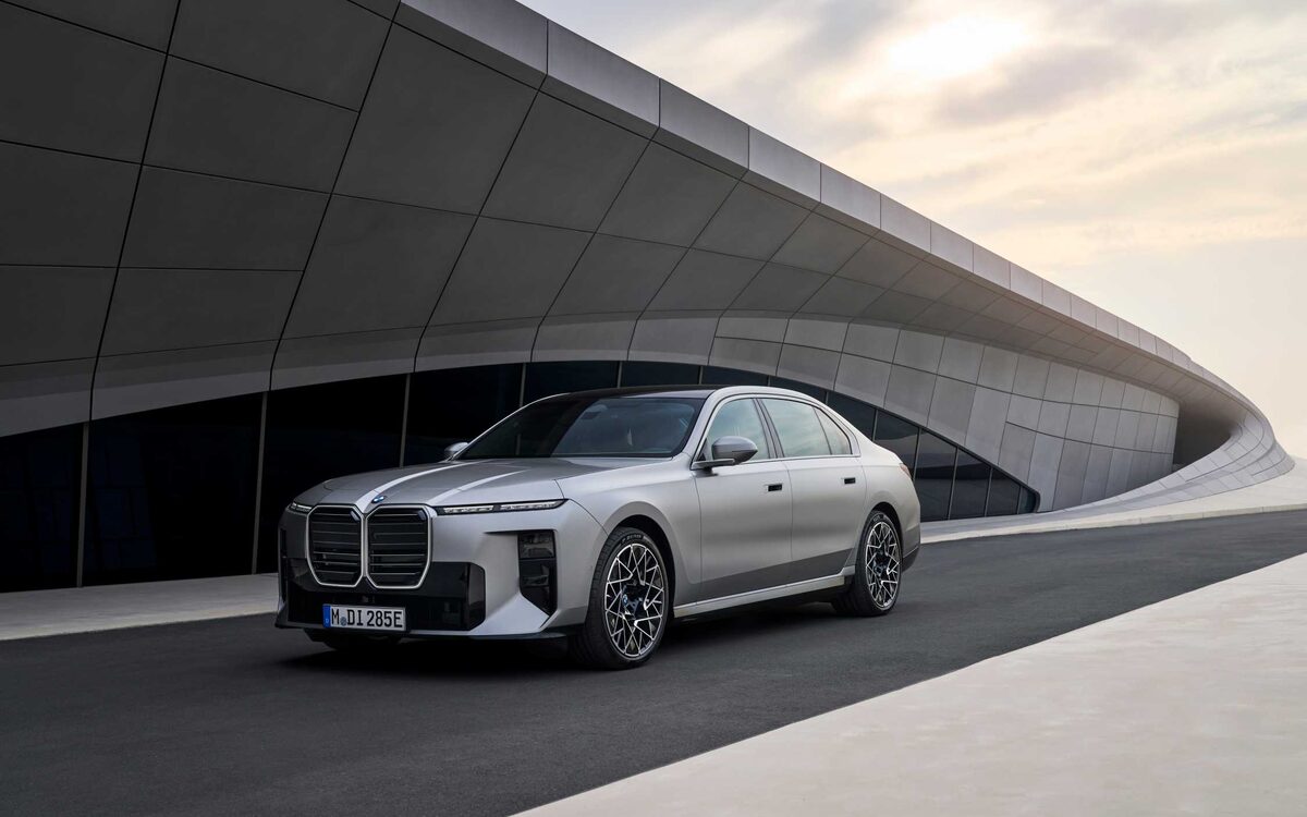 BMW i7 in silver, front three-quarter view beside a curved concrete building
