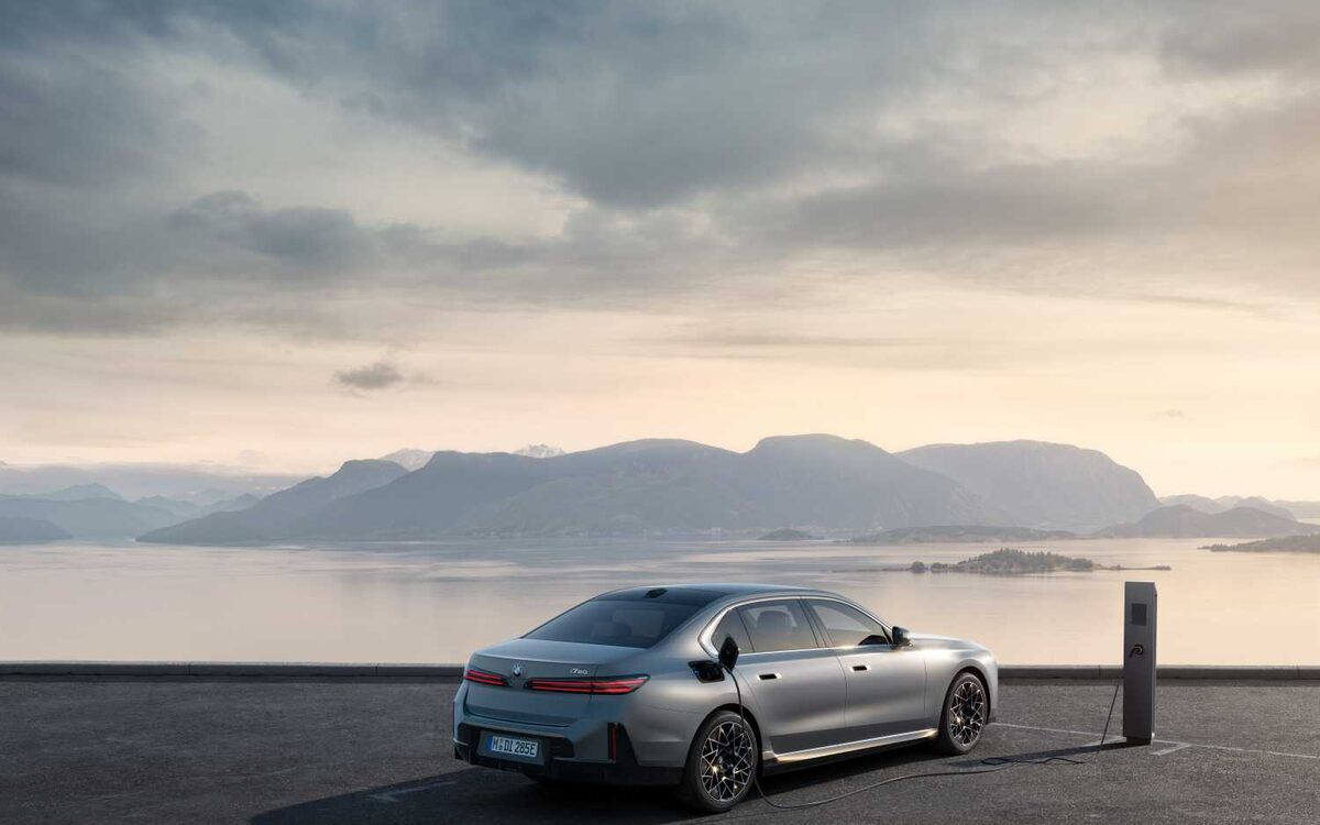 BMW i7 in grey, rear three-quarter view at a coastal charging point