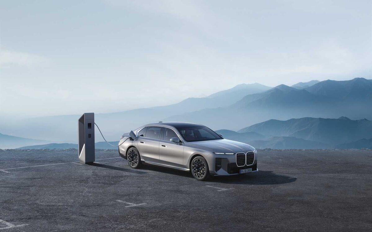 BMW i7 in grey plugged into a charger on a hilltop with mountains behind