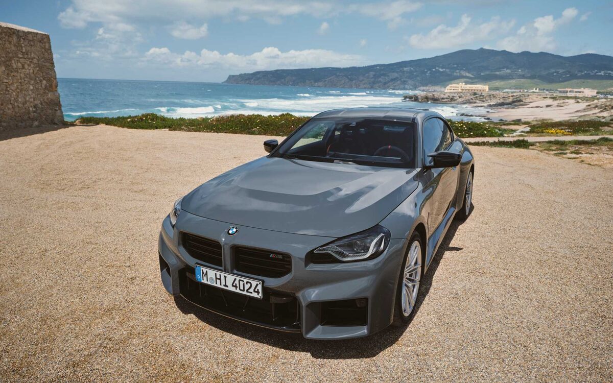 BMW M2 in grey, front three-quarter view parked on a sandy coastal lookout