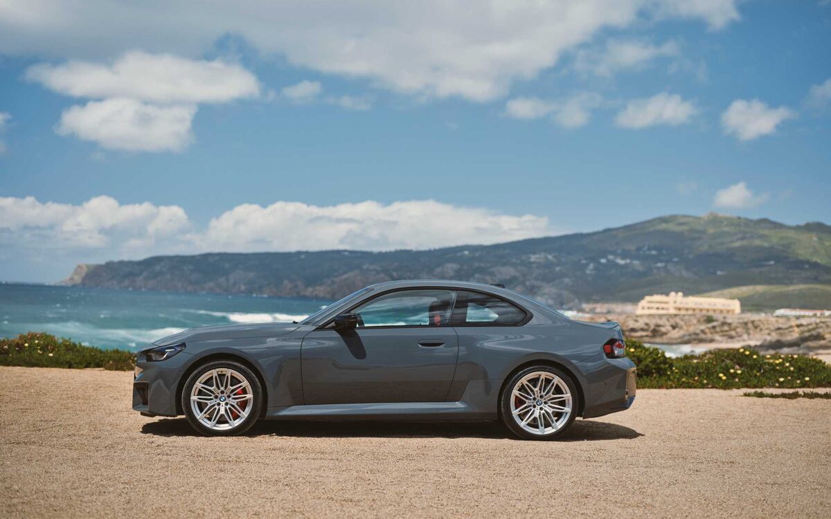BMW M2 in grey, side profile with sea and hills behind