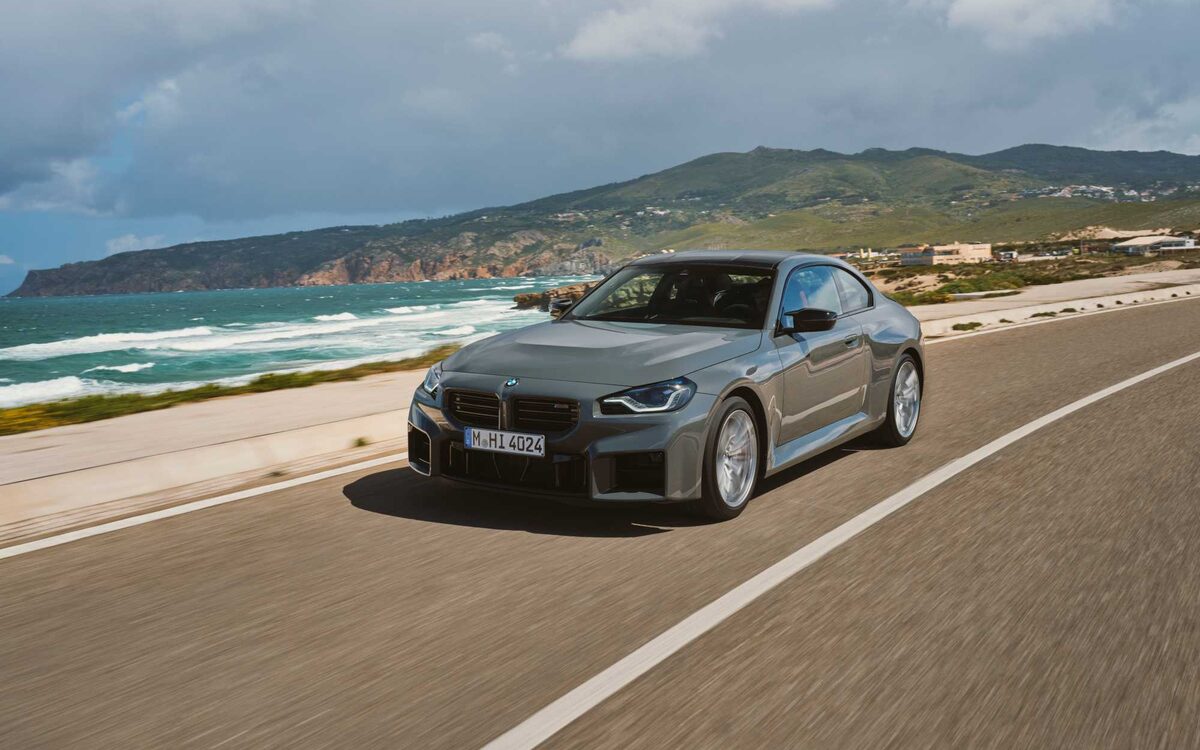 BMW M2 in grey driving along a coastal road, front three-quarter view