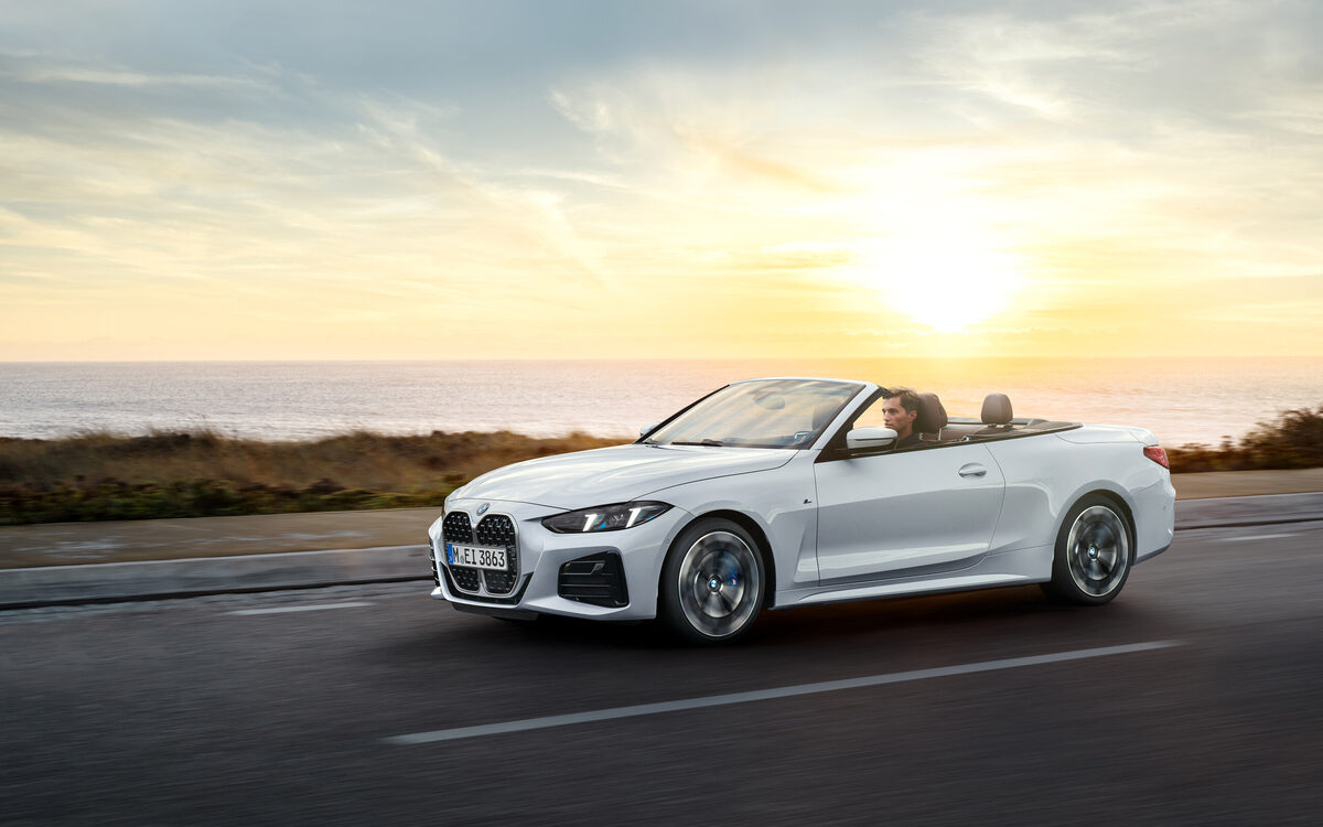 BMW 4 Series Convertible in white with the roof open at sunset, front three-quarter view