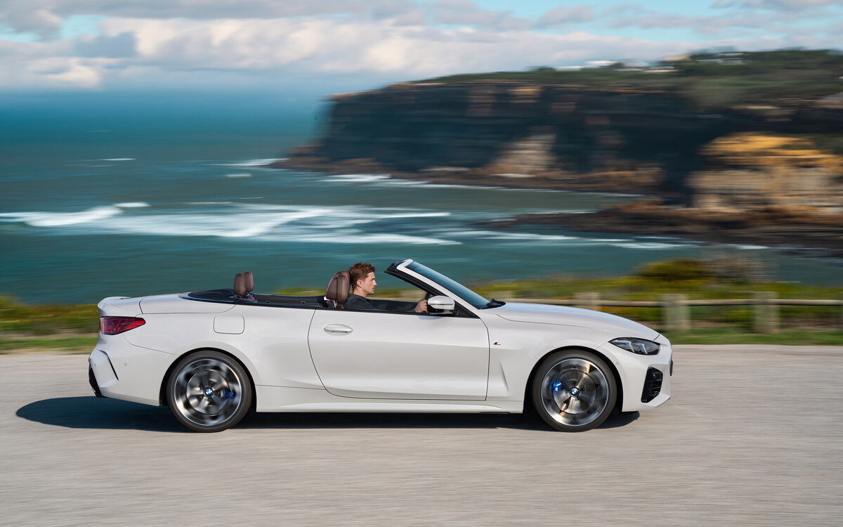 BMW 4 Series Convertible driving with the roof open, side profile