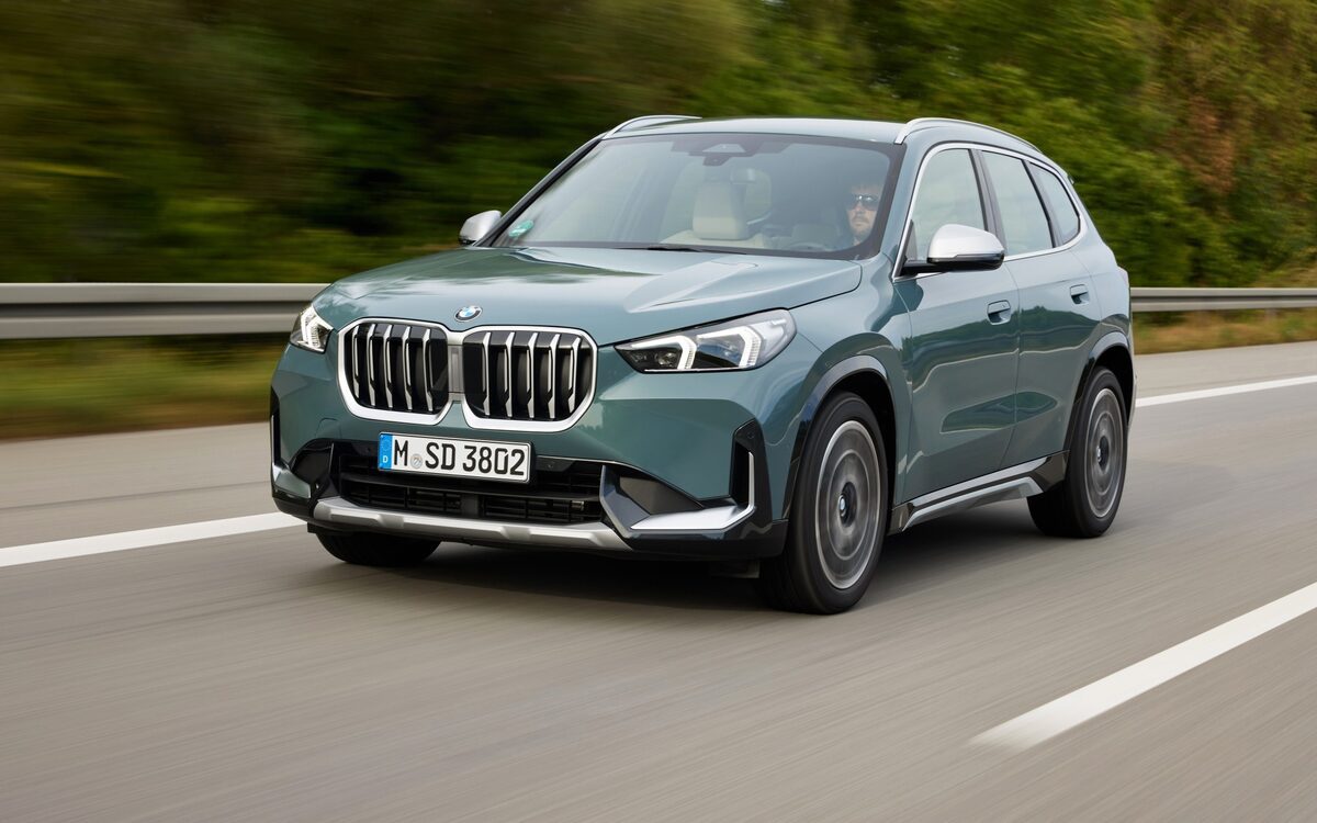 BMW X1 sDrive18d in teal-grey paint driving on a country road, seen from the front three-quarter