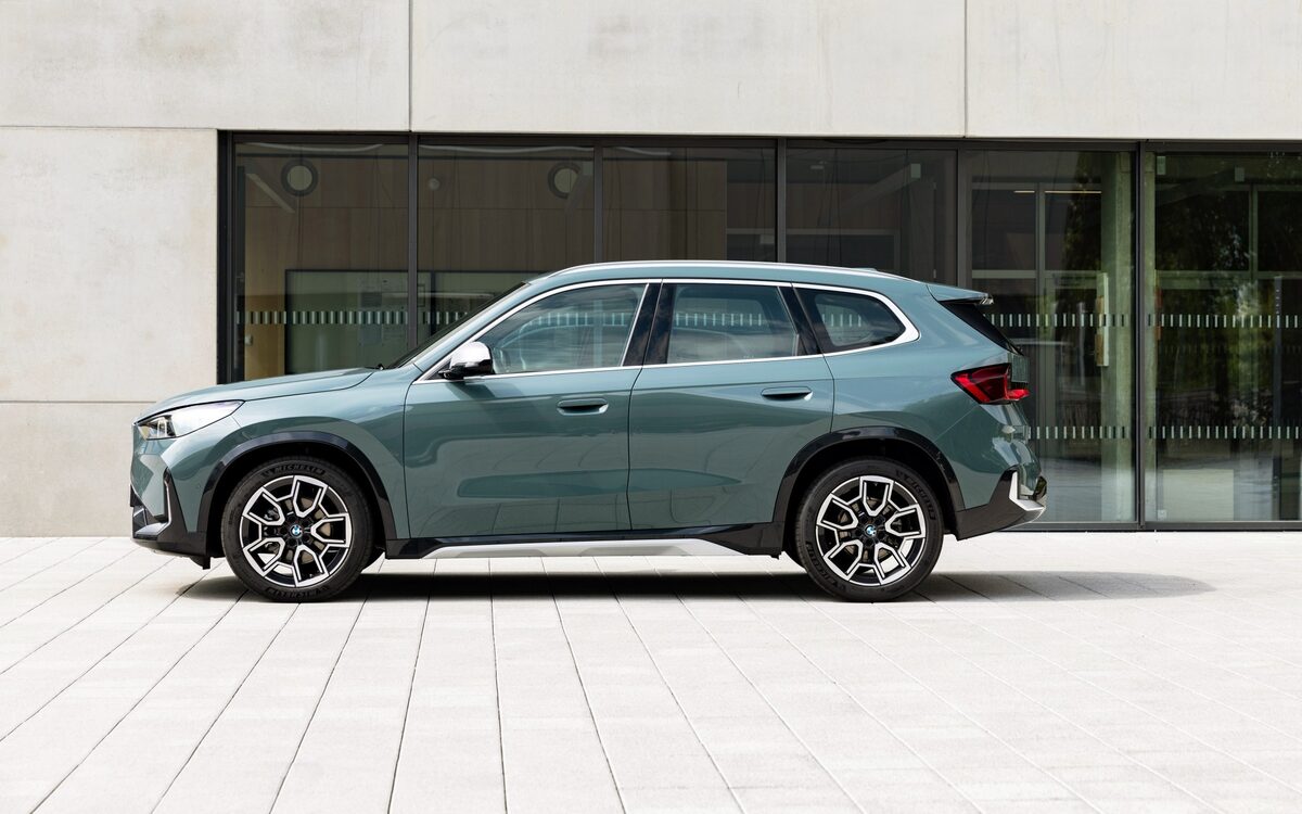 BMW X1 sDrive18d in teal-grey paint parked in side profile in front of a glass-fronted building