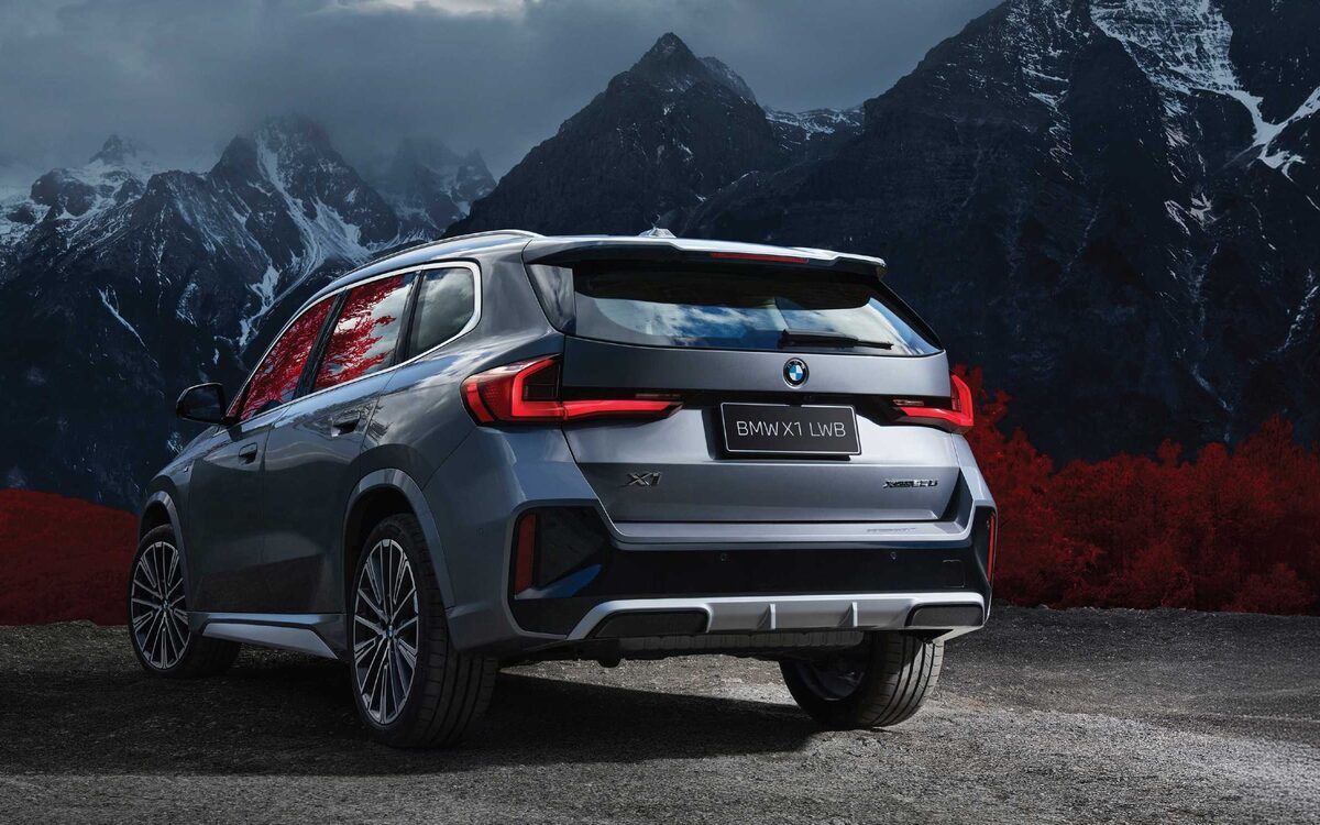 BMW X1 LWB in grey seen from the rear with the tail lamps lit, snow-capped mountains behind