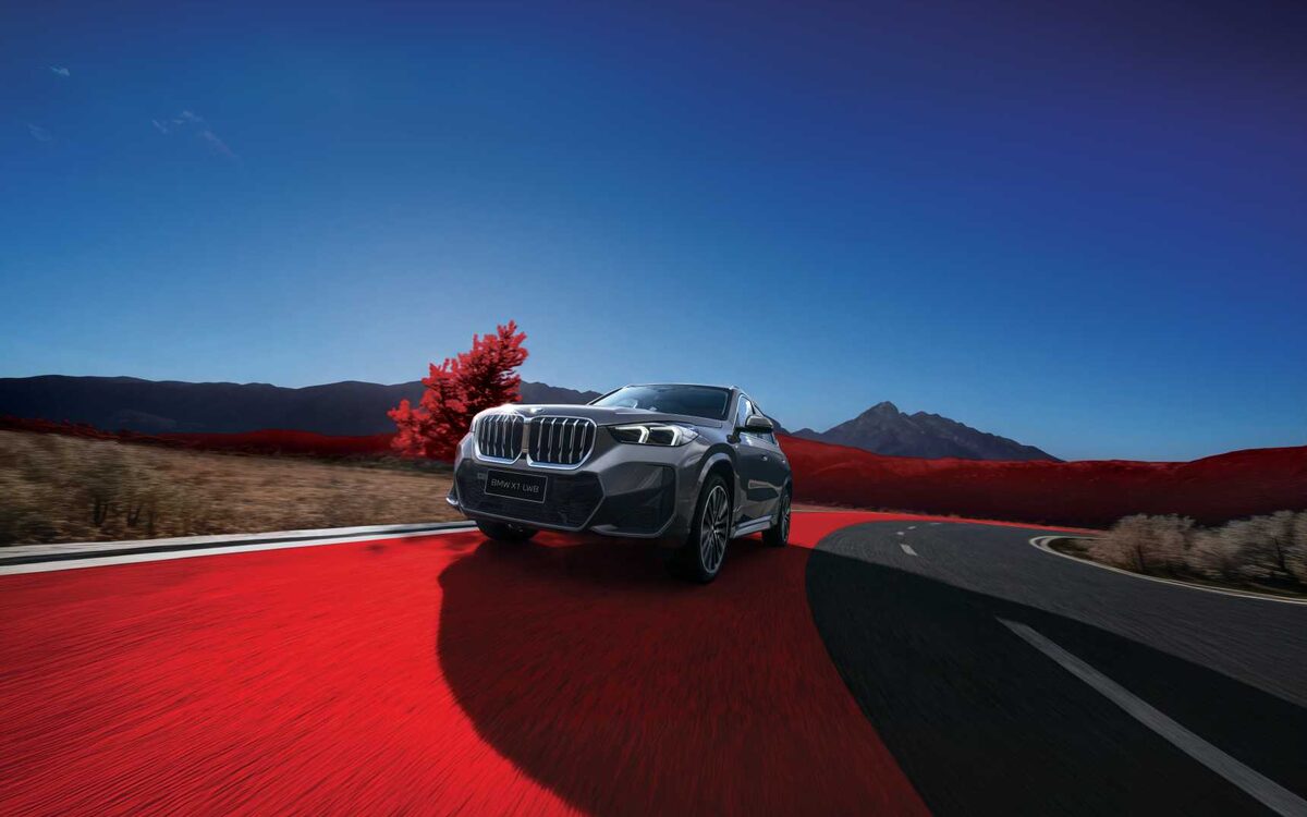 BMW X1 LWB in grey driving towards the camera on a long road under a deep blue sky