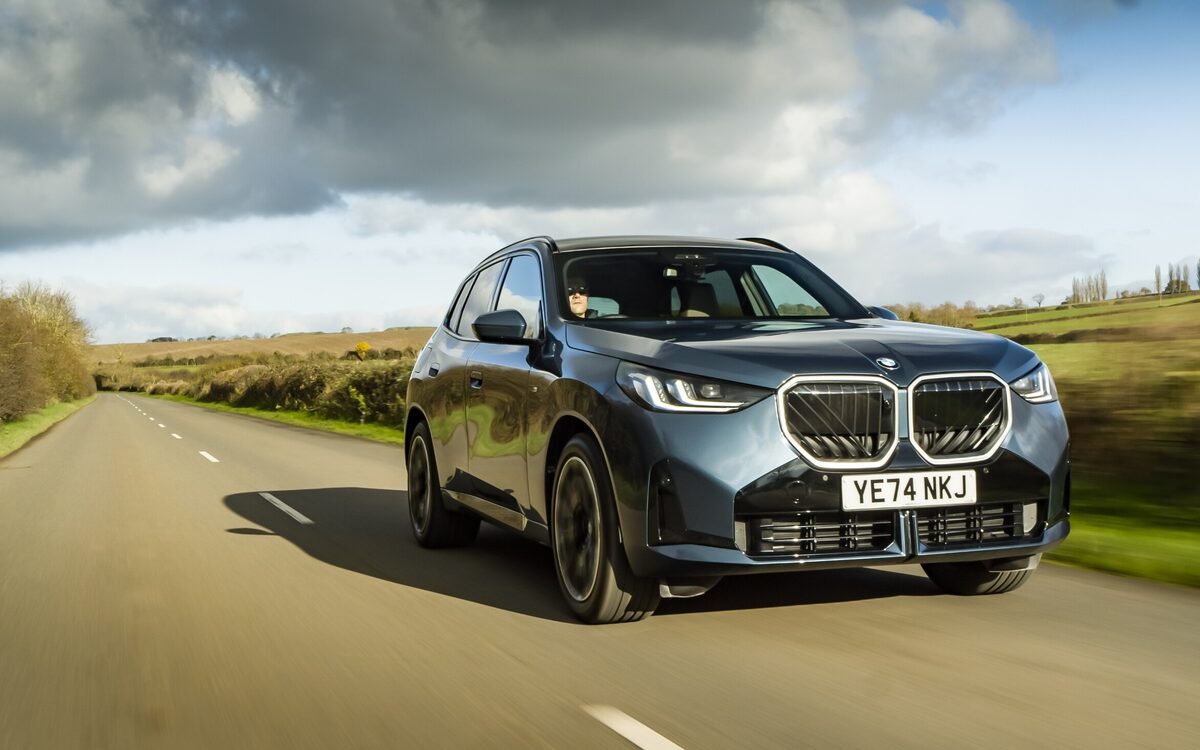 BMW X3 in blue-grey paint driving towards the camera on a country road