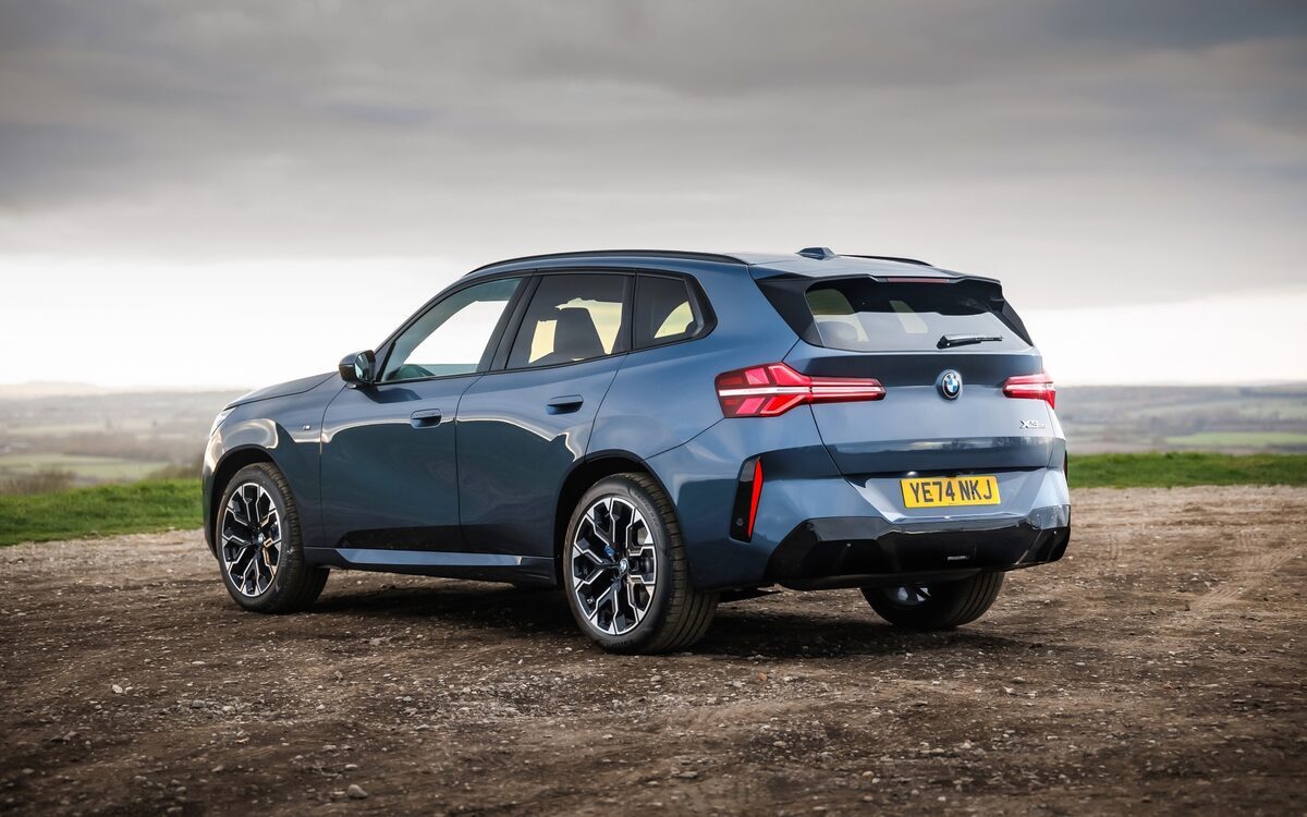 BMW X3 in blue-grey paint seen from the rear three-quarter parked on gravel at dusk