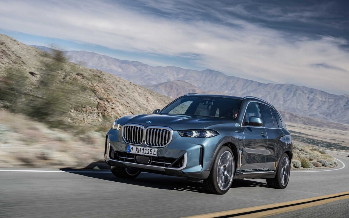 BMW X5 in blue driving on a desert mountain road, front three-quarter view